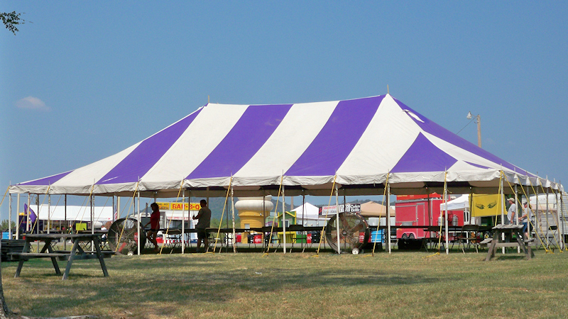 Purple striped tent canopy with tables and cooling fans.