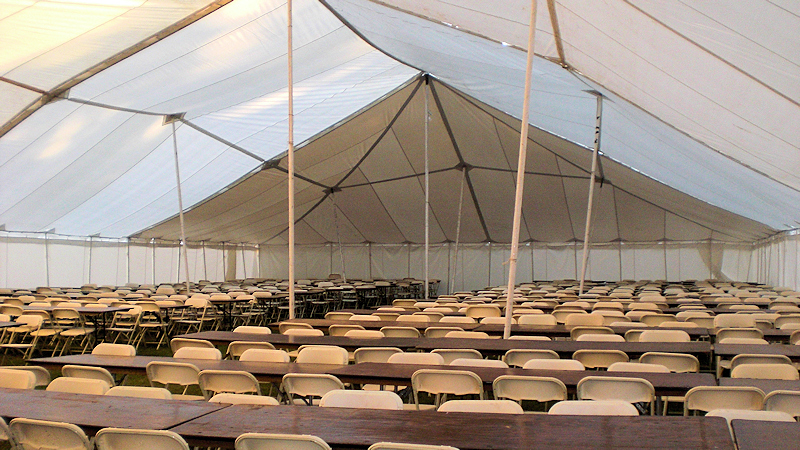 Interior of a tent with rows of tables and chairs.